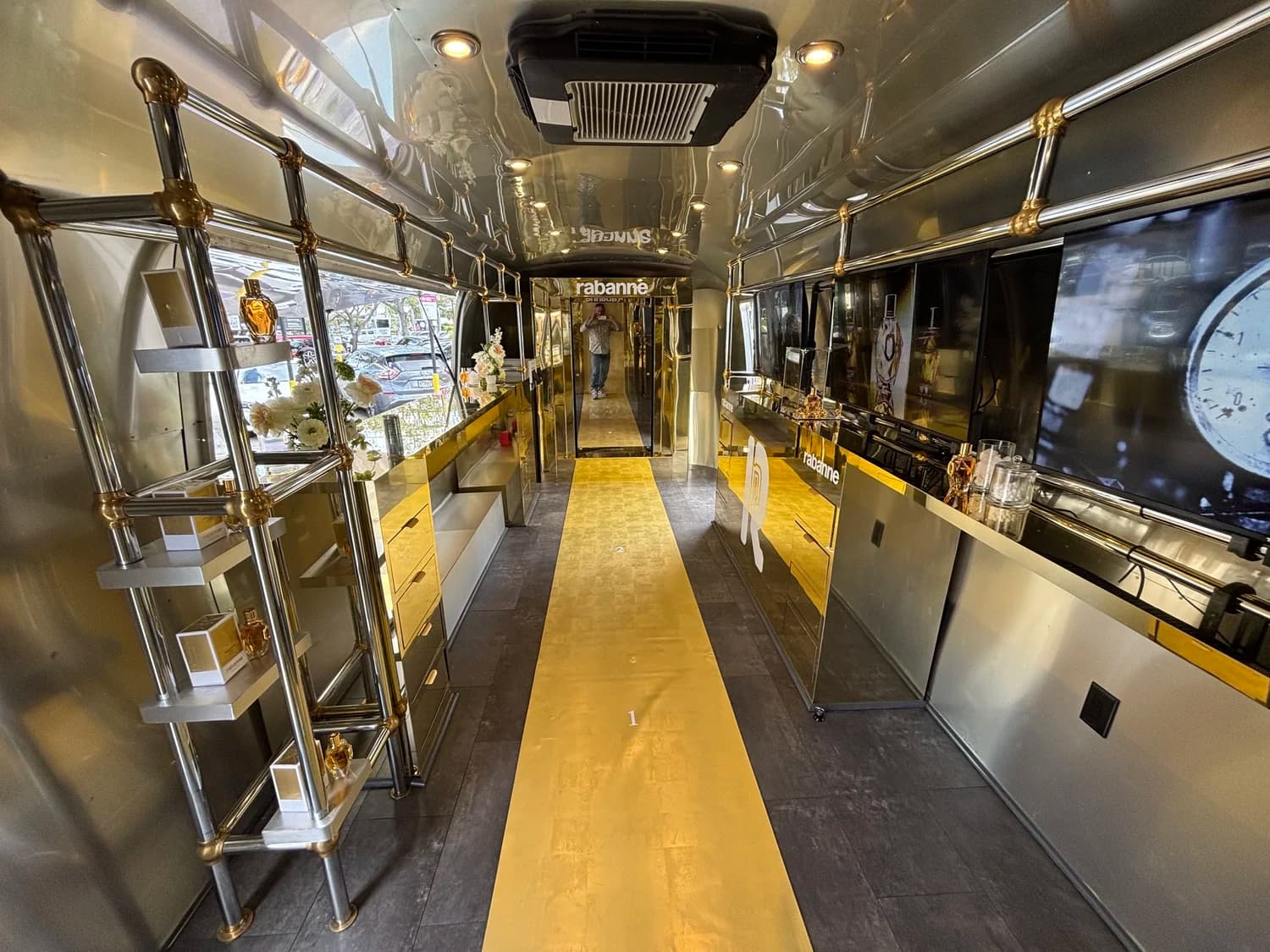Gold and chrome interior of the Rabanne Airstream activation trailer with display shelving and screens