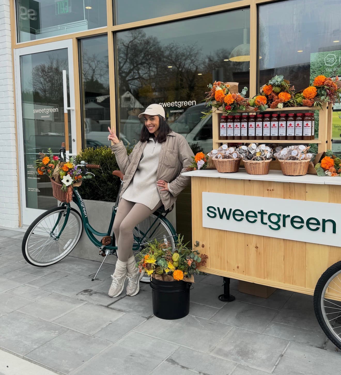 Custom wooden Sweetgreen apple cider cart with fall florals and a branded green bicycle outside a Sweetgreen storefront